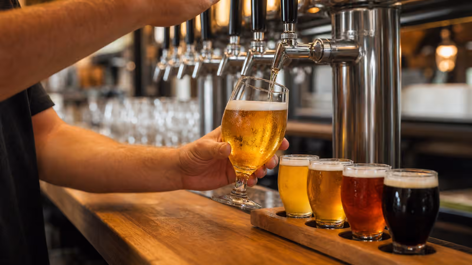 A bartender pouring golden draft beer beside a small flight of beer samples on a clean taproom bar.