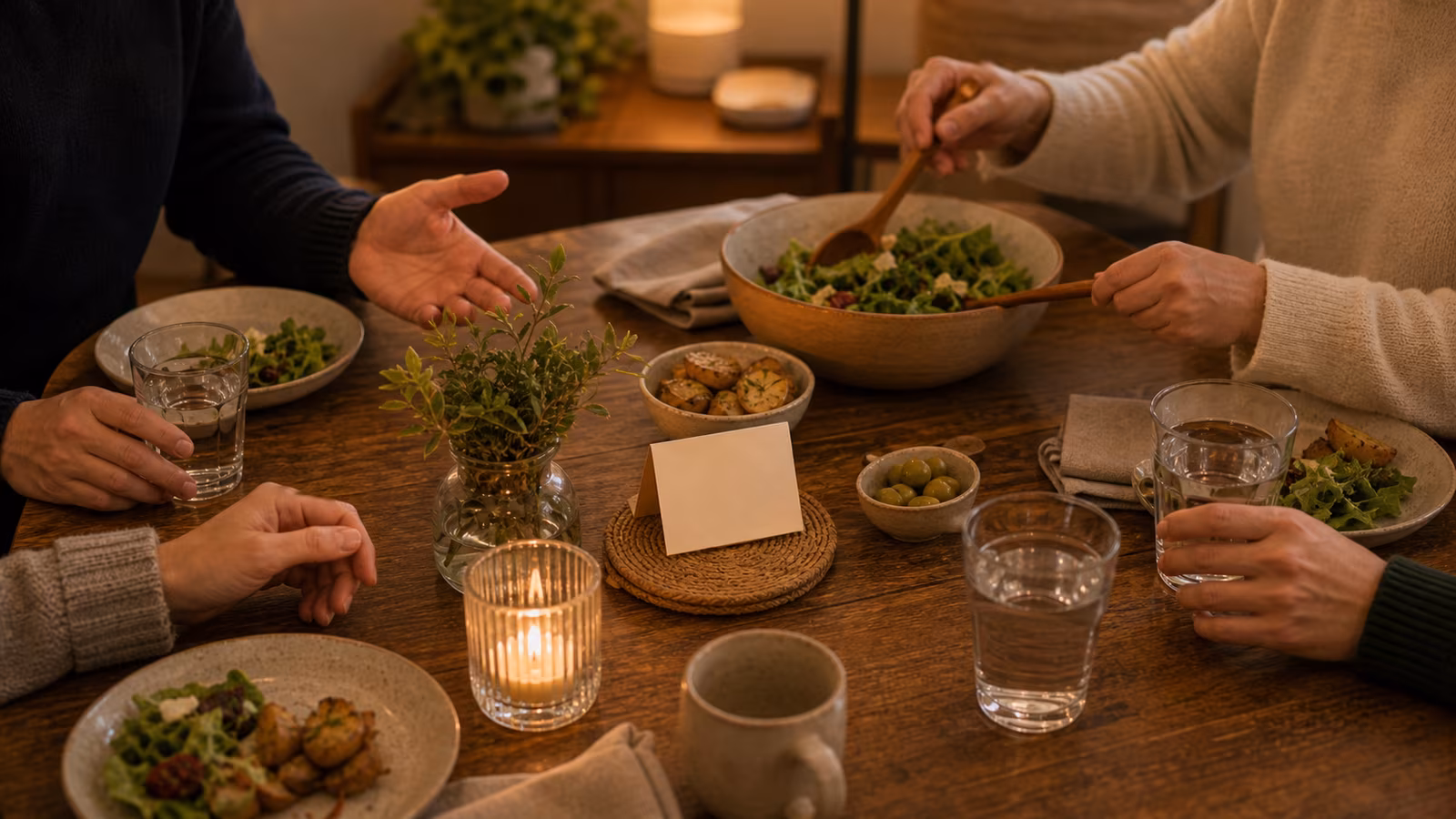 a dinner table with a small conversation card, hands gently turning toward a shared dish, and a calm host presence