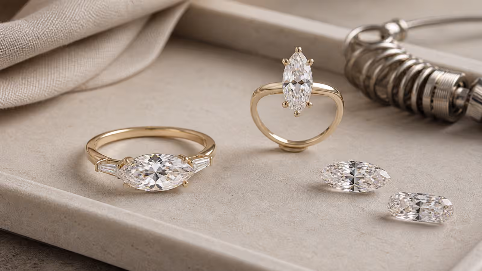 East-west engagement ring with an elongated center stone beside sample mounts and loose stones.