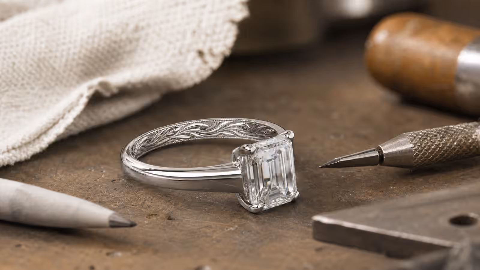 Engagement ring with subtle engraved detail beside jeweler's tools and a polishing cloth.