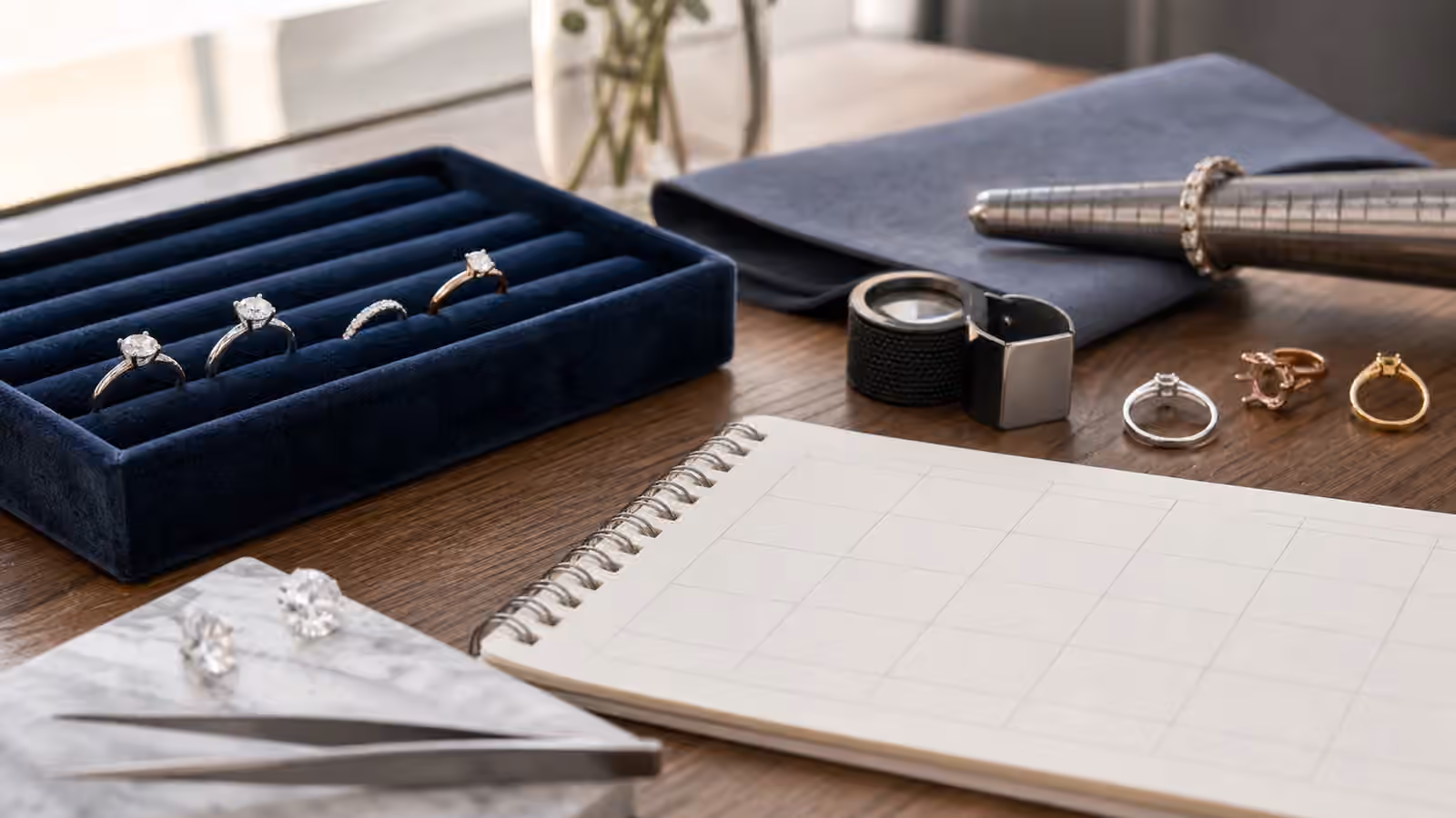 Engagement ring samples, loupe, ring sizer, and blank planning calendar on a jeweler's desk.