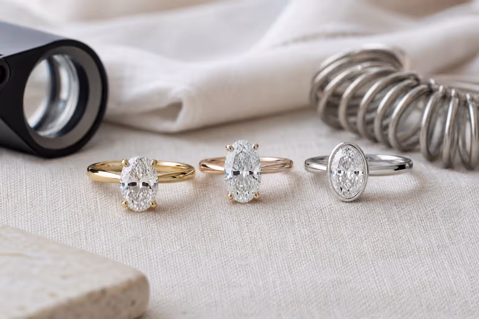 Three oval diamond engagement rings compared beside a loupe and sizing tools.