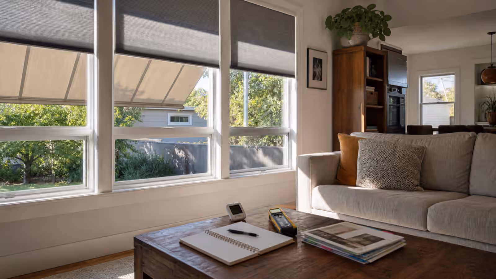 A bright living room with shaded windows, cellular shades, a notebook, room thermometer, and infrared thermometer.