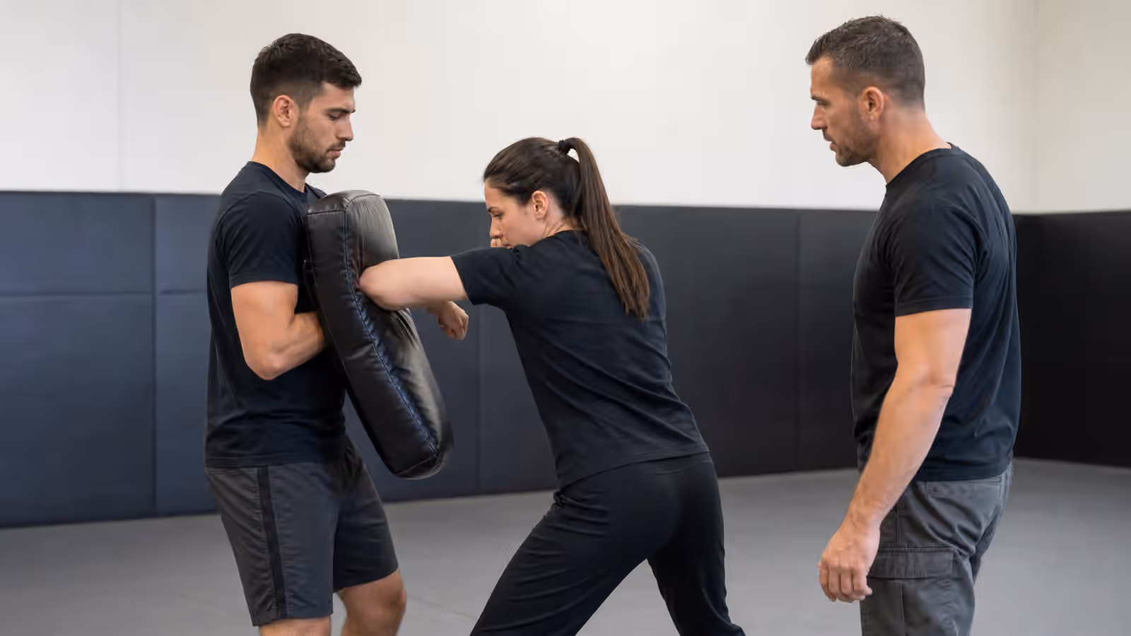 Adult Krav Maga students practicing a controlled elbow-strike pad drill while an instructor observes.