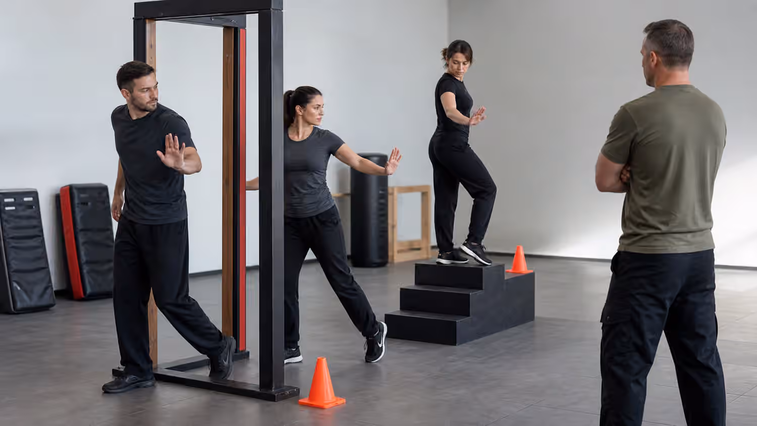 Krav Maga students practice calm open-hand positioning near a training doorway and stair-step prop.
