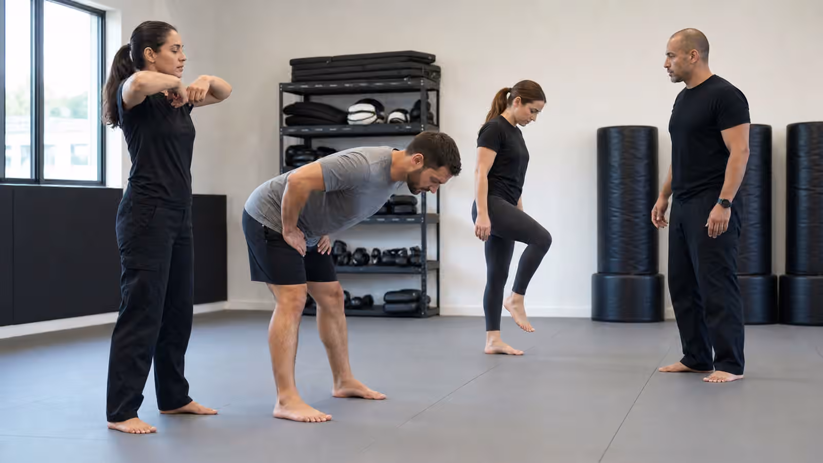 Adult Krav Maga students doing controlled mobility drills while an instructor watches spacing on a clean training floor.