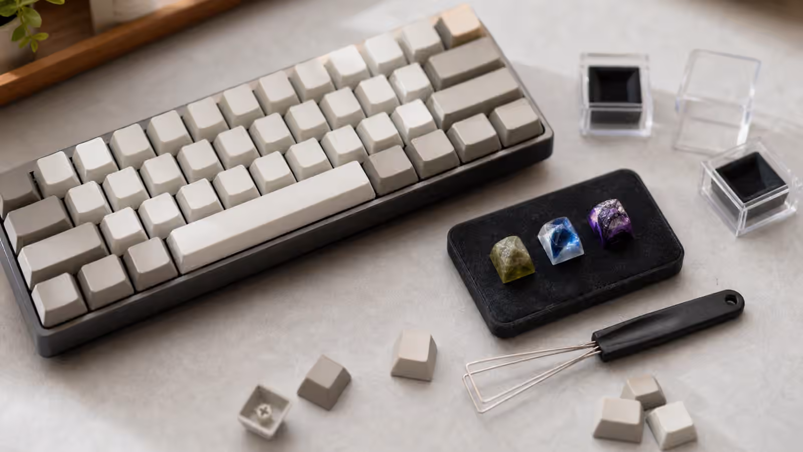 Artisan keycaps on a small display tray beside a compact mechanical keyboard and keycap puller.
