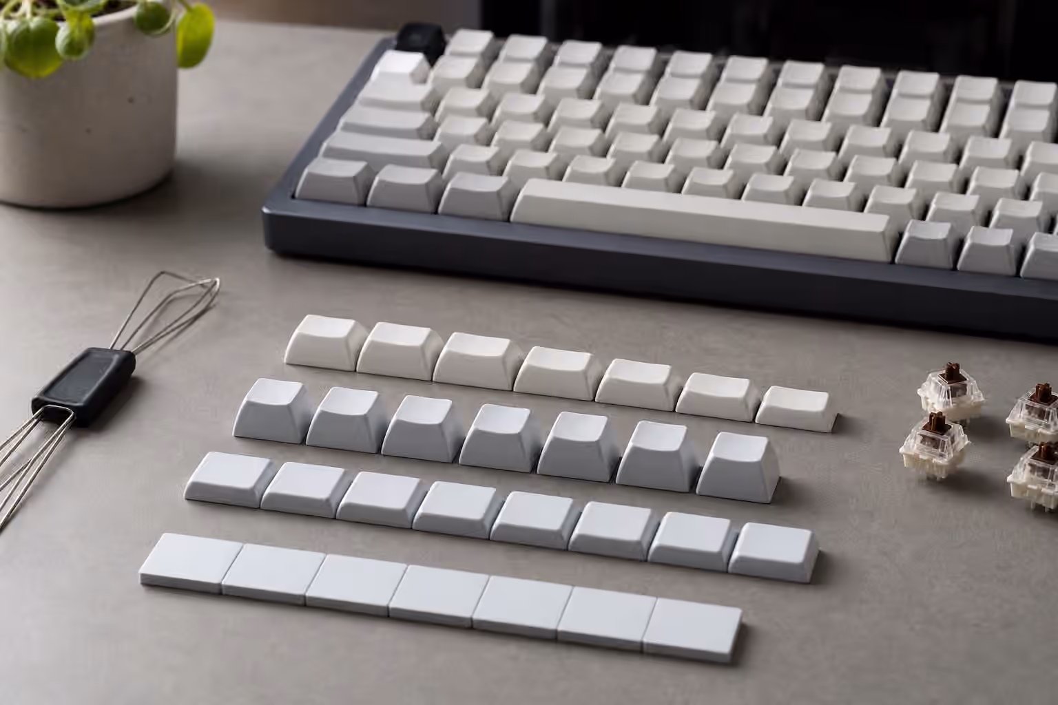 Rows of blank mechanical keyboard keycaps arranged to show different profile heights beside switches and a keyboard.