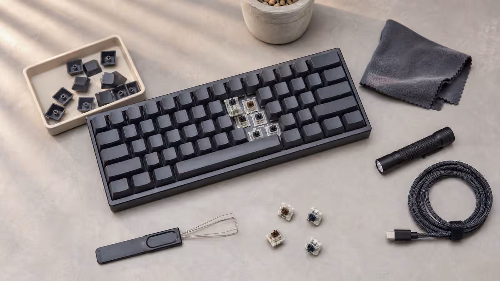 Used mechanical keyboard with several keycaps removed beside a flashlight, cloth, cable, and switch tools.