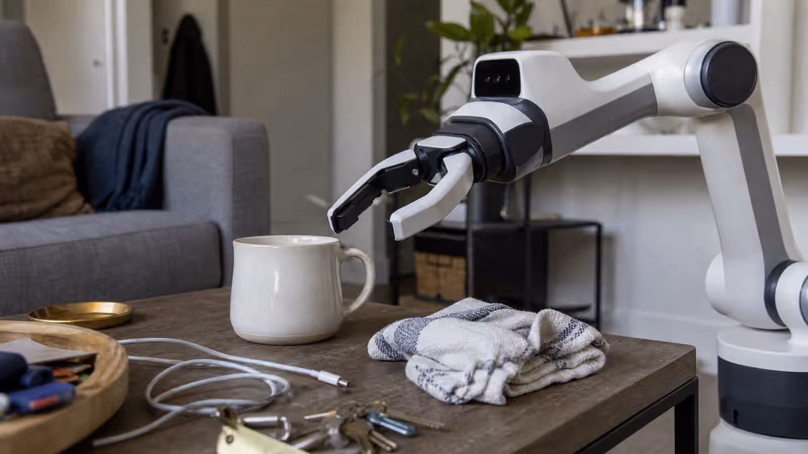 Robot gripper reaching toward a mug amid ordinary household clutter