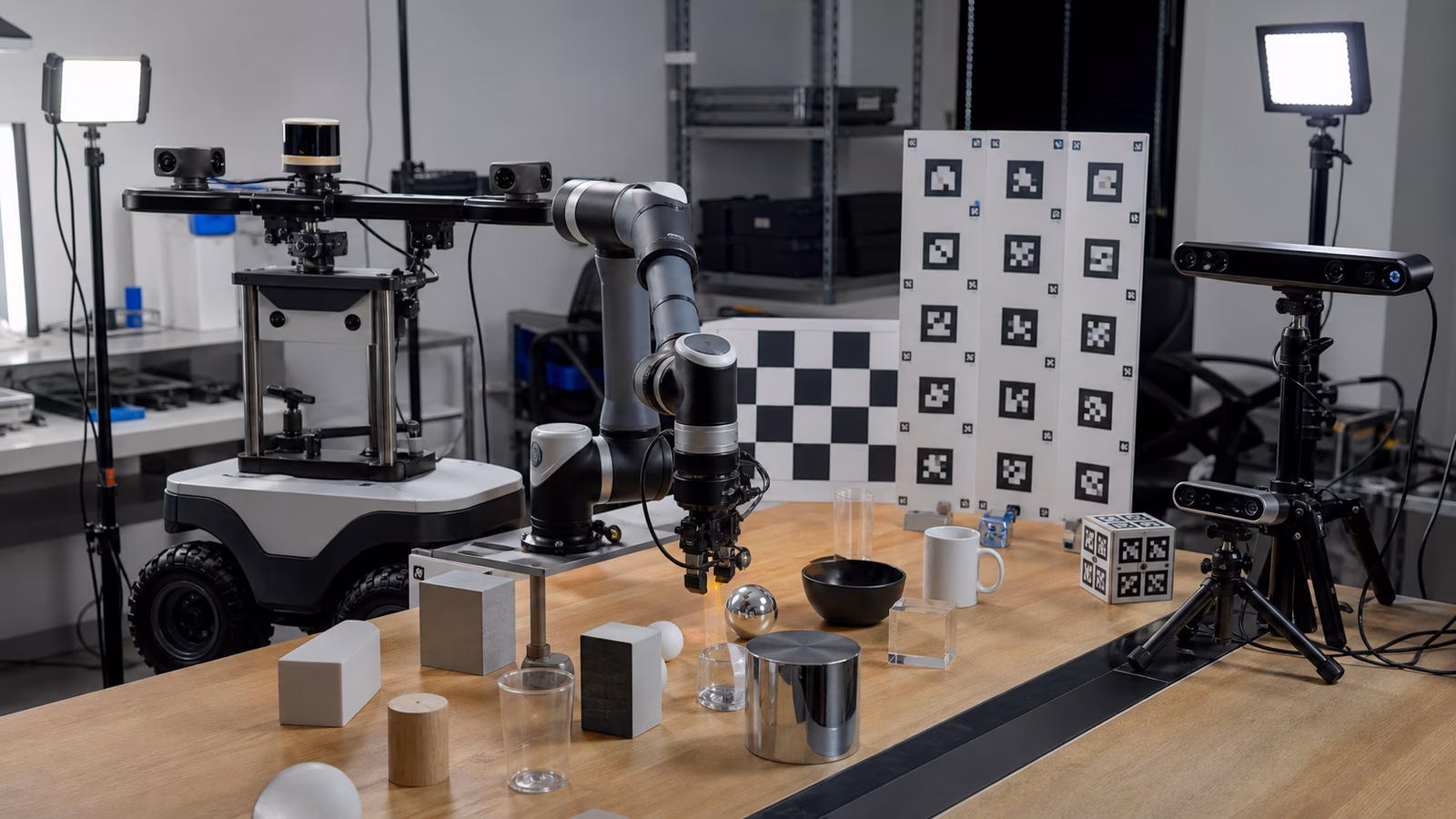 A robot perception lab bench with a mobile base, robot arm, cameras, lidar, calibration boards, lights, and test objects.