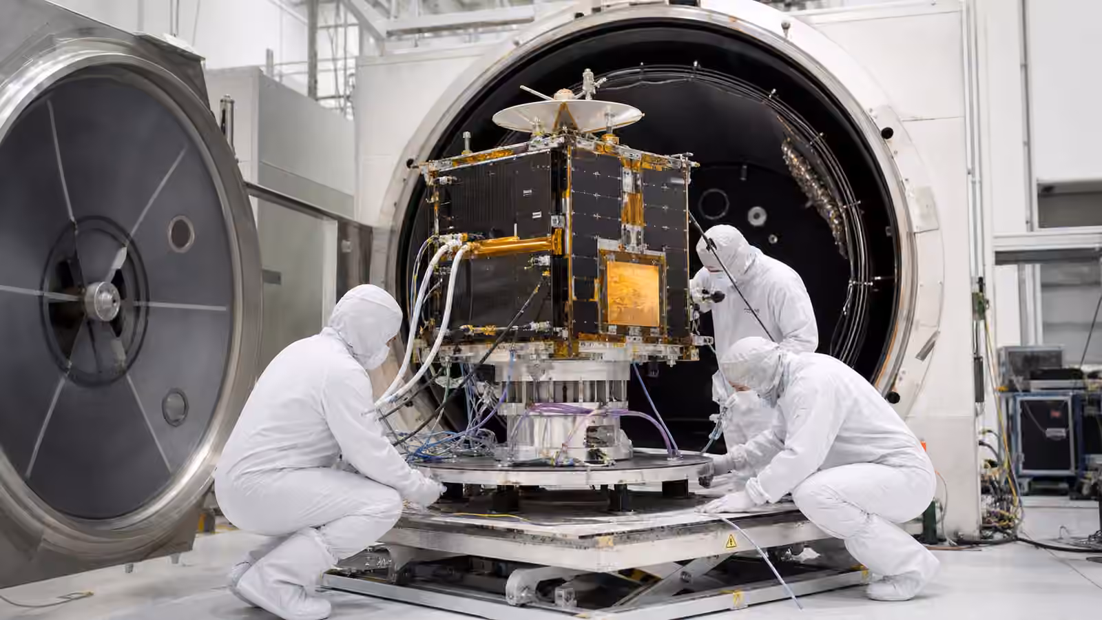 Cleanroom technicians prepare a compact satellite for thermal vacuum testing inside a large chamber